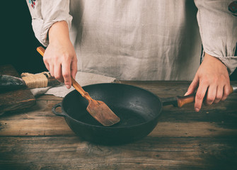 women's hands hold a round black pan and a wooden spatula