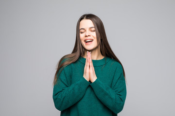 Young pretty woman pray wearing in green sweater isolated on gray background