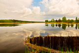 Fototapeta Natura - Calm lake surrounded by spring forest. Reflection of thunder clouds in the water.