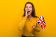 © Asier - Young european woman holding an united kingdom flag shouting excited to front.