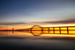 Long silhouetted bridge with an arch crossing a crystal clear calm body of water at sunset. Perfect reflections in the water - Long Island New York.  