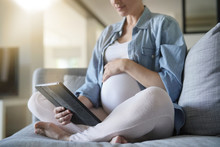 Pregnant Woman Using Digital Tablet, Relaxing In Couch