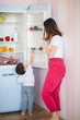 © Olena Serzhanova - Little boy trying to pick something from fridge while his mother opening the fridge door.