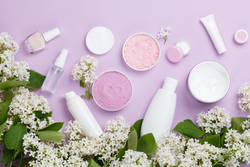 Wall Mural - Skin care products (tonic or lotion, serum, cream, micellar water, sea salt, cotton pads) on purple background with spring white lilac blossom. Freshness natural anti-age care. Female spa cosmetics