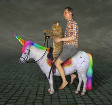 The Barefoot Man With His Cat  Is Riding Together On The Real Unicorn Along A Cobbled Road In The Evening.