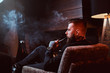Bearded handsome man is sitting near fireplace and smoking hookah, making good misty vapour.