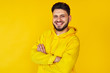 © Davidovici - Young hipster male in yellow hoodie smiling and posing with arms crossed over yellow background