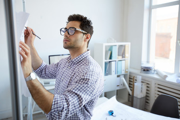 Waist up portrait of young engineer  making notes on plan  in office, copy space