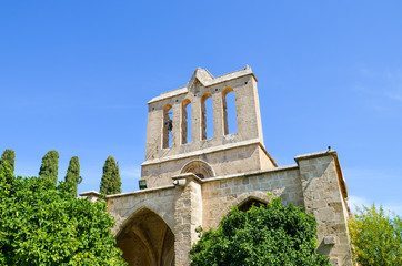 Historical building in Cypriot Bellapais Abbey complex in city Bellapais, Turkish Northern Cyprus taken from below with blue sky above and green trees around. Popular tourist spot