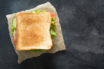 Sandwich with bacon, tomato, onion, salad on black background.