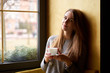 © Kiryl Lis - Cute smiling girl with long hair siting near the window and drinking coffee or tea  in the cafe.