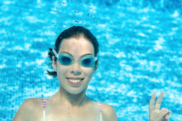 Child swims underwater in swimming pool, happy active teenager girl dives and has fun under water, kid fitness and sport on family vacation on resort