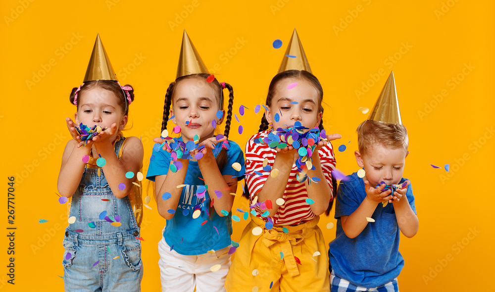 happy children on holidays  jumping in multicolored confetti on yellow - obrazy, fototapety, plakaty 