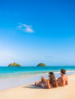 © Maridav - Beach vacation couple relaxing sunbathing on hawaiian tropical beach in Lanikai, Oahu, Hawaii, USA. American people on summer holidays sun tanning lying down on sand.
