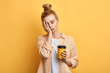 Tired Sleepy Woman Holds A Cup Of Coffee, Has Sad Expression, Closes Eyes, Cannot Wake Up In The Morning And Go To Work. Difficult, Hard Monday. Isolated Yellow Background