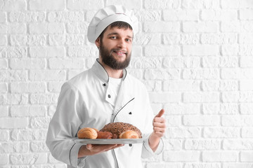 Poster - Young chef with fresh bakery products showing thumb-up gesture on white brick background