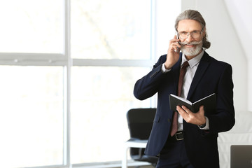 Canvas Print - Handsome mature businessman talking by mobile phone in office