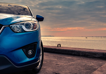 Blue compact SUV car with sport and modern design parked on concrete road by the sea at sunset in the evening. Hybrid and electric car technology concept. Car parking space. Automotive industry.