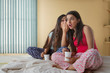 © IndiaPix - Two young girls sitting on bed at home holding coffee mugs and gossiping