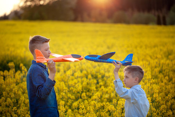 Wall Mural - Two toys airplanes in hands boys looking at each other in yellow field on summer day.