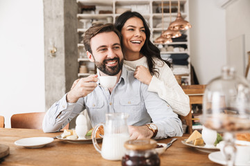 Wall Mural - portrait of brunette european couple eating at table while having breakfast in kitchen at home