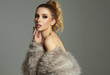 © kiuikson - Photo of blond female model with faux fur and tied hair looking at camera isolated on gray background