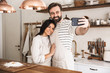 © Drobot Dean - Portrait of positive couple man and woman 30s wearing aprons taking selfie photo while cooking at home
