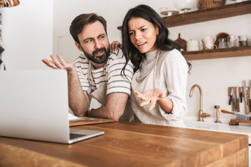 Sticker - Portrait of pretty couple looking at laptop while cooking pastry in kitchen at home