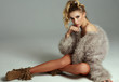 © kiuikson - Photo of blond female model with faux fur and tied hair looking at camera isolated on gray background