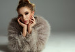 © kiuikson - Photo of blond female model with faux fur and tied hair looking at camera isolated on gray background