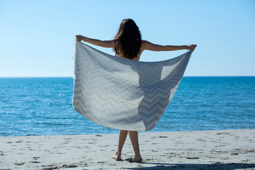 Pretty young girl wrapped in beach towel poses to camera. Full length photo shoot and wonderful hair. Healthy, beauty and summer holiday concept.