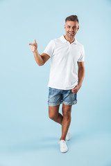 Poster - Handsome excited emotional adult man posing isolated over blue wall background pointing.