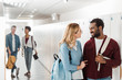 © LIGHTFIELD STUDIOS - smiling multiethnic students looking at each other in corridor in college