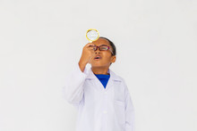 Young Preteen African American Kid Wearing Lab Coat Looking Up With Magnifier In White Isolated Background. Can Be Doctor Or Scientist.