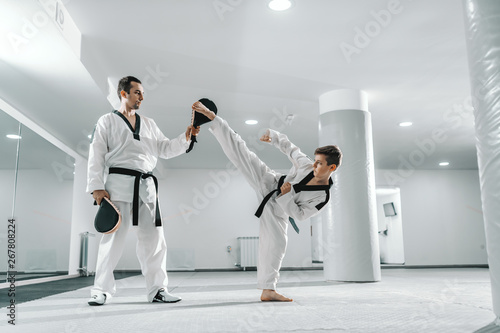 Dekoracja na wymiar  mlody-chlopiec-kaukaski-w-dobok-kopiac-boso-podczas-gdy-trener-trzyma-cel-kopniecia-taekwondo