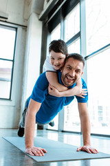 Wall Mural - happy father doing push up exercise with son on back at gym