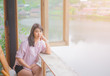 © otello-stpdc - Portrait of Beautiful Asian Woman. Sitting on Wooden chair. Table near the window. Casual wearing pink shirt. With sunlight of the morning. atmosphere Lagoon. feeling enjoy relaxed. Smiling Happy.