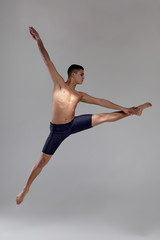 Photo of a handsome man ballet dancer, dressed in a black shorts, making a dance element against a gray background in studio.