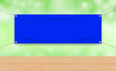 Wall Mural - vinyl blank blue on green bokeh background and wood plank table, mock up textile fabric empty for banner advertising stand hanging, indoor outdoor fabric vinyl backdrop for copy space presentation ad