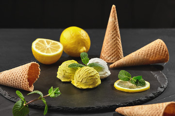 Wall Mural - Tasty creamy and lemon ice cream decorated with mint served on a stone slate over a black background.