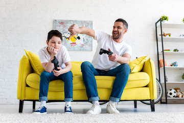 Wall Mural - father showing thumb down while sitting with son and playing Video Game at home