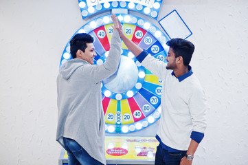 We are millionaires! Very excited two young asian guys against fortune wheel win at lottery big prize. Give high five each other.