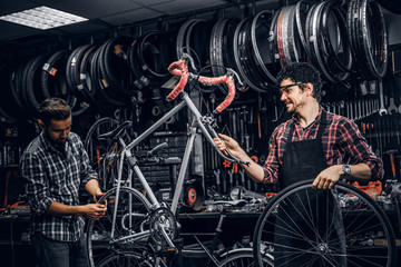 Wall Mural - Good teamwork of two nice mans at busy bicycle workshop. Mans are wearing checkered shirts.