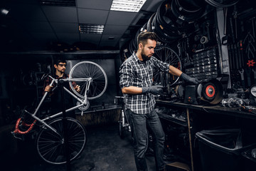 Wall Mural - Attractive pensive man is working with machine at busy bicycle workshop.