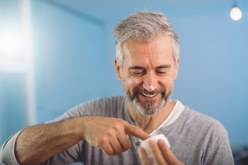 middle aged gray haired man putting face cream