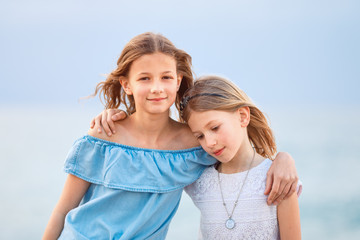 Two young girls wearing casual summer clothing looking, smiling at camera in a coastal region