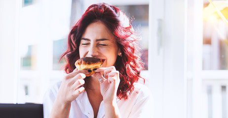 Cheerful young pretty woman enjoying while eating donuts