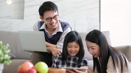 Wall Mural - Happy Asian family using tablet, laptop for playing game watching movies, relaxing at home for lifestyle concept