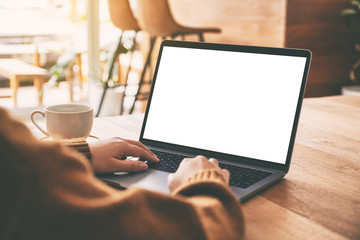 Mockup image of a woman using and typing on laptop computer with blank white screen and coffee cup on wooden table