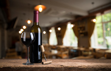 Red wine tasting in the wine cellar: wineglass and bottles next to the window and panoramic view of vineyards at sunset